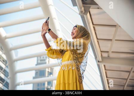 Donna islamica che utilizza l'app per smartphone organizza programmi focalizzati sullo smartphone mano musulmana moderna città degli emirati arabi uniti. La donna araba indossa hijab e musl Foto Stock