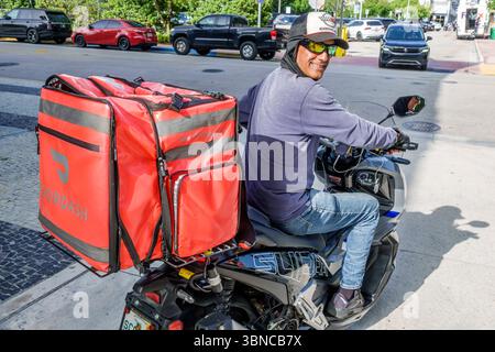 Miami Beach, Florida, uomo ispanico, consegna Doordash, corriere adulto che torna sorridente, zaino rosso con logo, casco nero con sole Foto Stock
