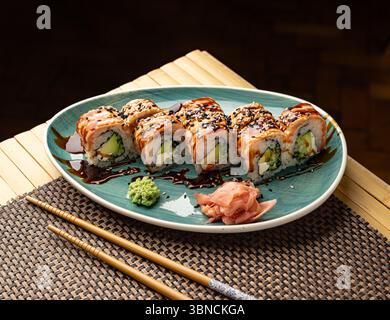 Deliziosi sushi con salmone, avocado, formaggio spalmabile, semi di sesamo e salsa di soia su un piatto Foto Stock