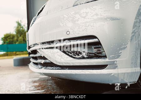 Vista ravvicinata di un'auto color argento ricoperta di bolle di sapone durante un autolavaggio, evidenziando l'importanza della pulizia e della cura del veicolo per la manutenzione Foto Stock