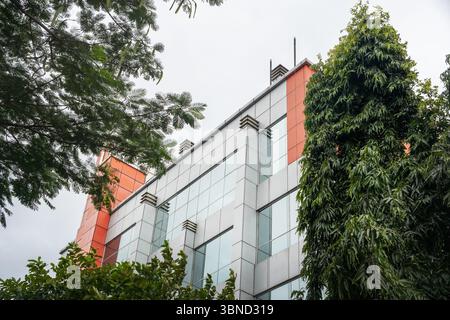 Alto edificio con un albero verde davanti. L'edificio e' fatto di vetro e ha un tetto rosso Foto Stock