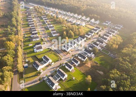 Vista aerea di un moderno complesso residenziale con case bianche identiche situate accanto a una foresta verde. Il quartiere residenziale è immerso nella Foto Stock