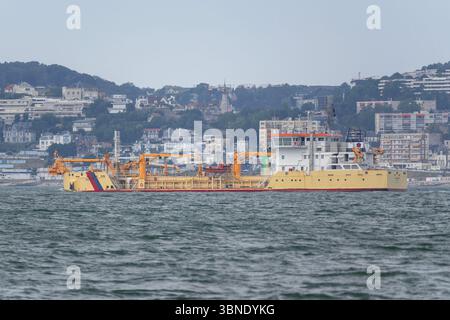 Le Havre, Francia - Vista sulla draga tramoggia JEAN ANGO che lascia il porto di le Havre con Sainte-Adresse sullo sfondo. Foto Stock