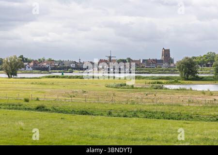 Una splendida vista panoramica della storica città di Woudrichem, Paesi Bassi, con la sua iconica chiesa e mulino a vento, annidata da un ampio fiume e lussureggiante Foto Stock