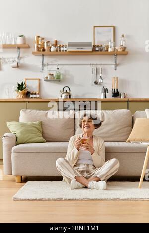 Una donna anziana siede comodamente sul pavimento, assaporando il suo drink e godendosi l'atmosfera intima. Foto Stock