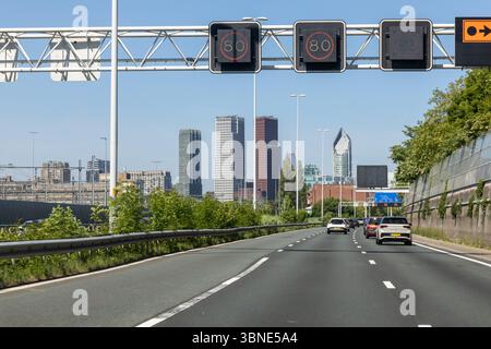 Autostrada urbana A12 che entra a l'Aia, Paesi Bassi, con moderni grattacieli sullo sfondo e auto che guidano sotto i segnali digitali del limite di velocità. Foto Stock