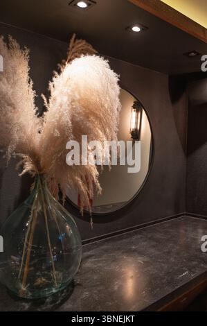 L'elegante design degli interni è caratterizzato da una splendida erba pampas elegantemente sistemata in un vaso accanto a un elegante specchio rotondo Foto Stock