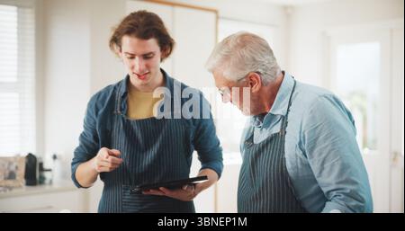 Uomini, chef e grembiule con tablet in cucina casalinga per l'ospitalità o l'abilità culinaria in cucina. Maturo, mentore o persona con aiuto, tecnologia o. Foto Stock