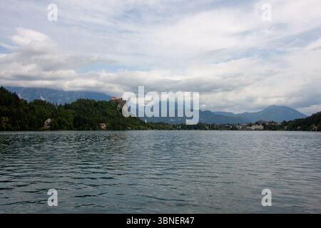 Una vista pittoresca del Lago di Bled è incorniciata da lussureggianti foglie verdi in primo piano, che offrono uno scorcio delle tranquille acque turchesi. Slovenia Foto Stock