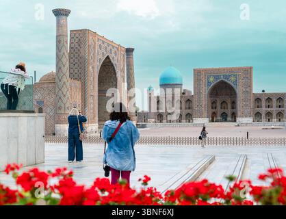 Vista posteriore di donne fotografate che scattano foto di madrasa in Piazza Registan a Samarcanda, Uzbekistan Foto Stock