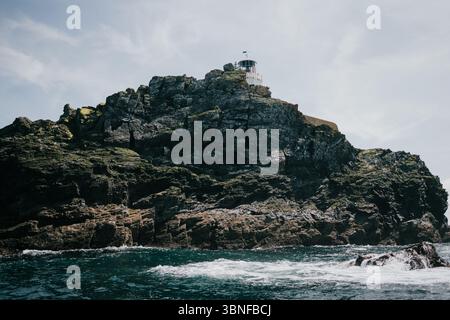Una scogliera rocciosa si affaccia sull'oceano. L'acqua è calma e il cielo è limpido. Il faro sulla scogliera è visibile in lontananza Foto Stock