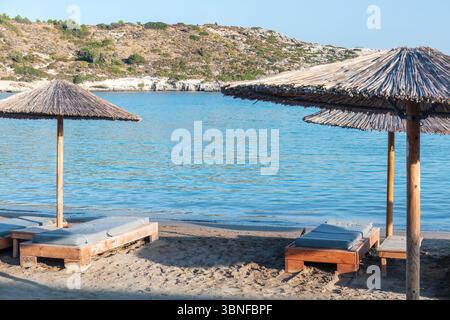 Rilassante spiaggia con ombrelloni di paglia e sdraio sulla spiaggia sabbiosa. Acque turchesi tranquille e onde dolci creano un'atmosfera serena Foto Stock