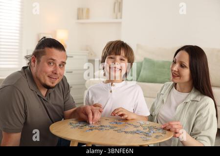 Genitori con loro figlio che risolvono il puzzle insieme a tavola al chiuso Foto Stock