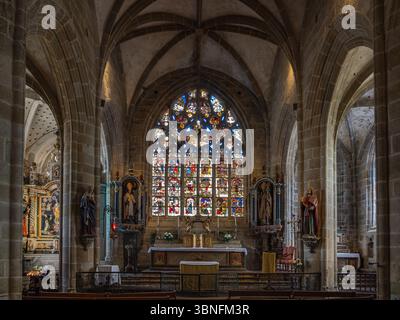 Coro della chiesa di Saint-Ronan del XV secolo a Locronan, Bretagna, con altare ornato, statue e vetrate colorate incorniciate da archi gotici. Foto Stock