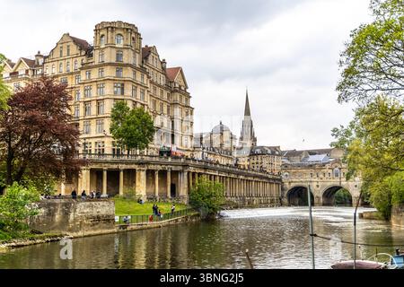 Bath, Regno Unito - 25 aprile 2025 - Empire Hotel e St. Michael's Spire sorgono sopra il fiume Avon con Pulteney Bridge e Weir nel centro storico Foto Stock