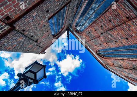 Vista dall'angolo basso di una storica chiesa in mattoni rossi con una lanterna e un suggestivo cielo blu pieno di soffici nuvole bianche. Foto Stock