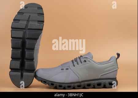 Le scarpe da atletica grigie presentano un design innovativo della suola e sono esposte su un caldo sfondo arancione. Foto Stock