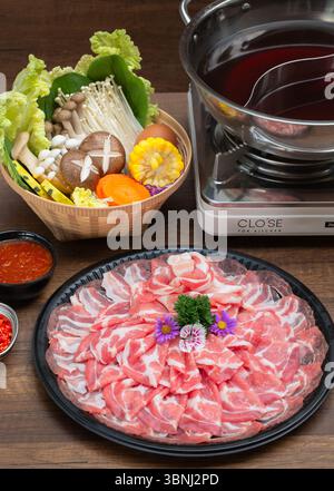 Un hot pot (shabu shabu) splendidamente organizzato in stile giapponese con carne di maiale a fette sottili disposte a forma di fiore su un vassoio nero, circondato da Foto Stock