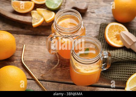 Vasetti Mason di succo d'arancia fresco con diversi agrumi e centrifuga su sfondo in legno Foto Stock