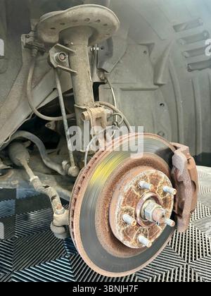 Disco freno arrugginito e molla a gas esposta sul mozzo della ruota del veicolo durante la riparazione. Foto Stock