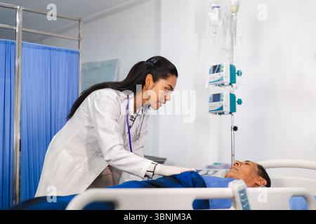 Un medico donna compassionevole in un cappotto bianco cura attentamente un paziente anziano in un letto d'ospedale, garantendo comfort e monitoraggio equi medico Foto Stock
