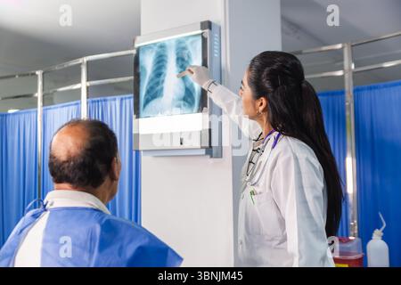 Un medico donna che indossa un cappotto bianco e uno stetoscopio discute una radiografia con un paziente maschio anziano in un ambiente medico. L'immagine trasmette l'assistenza sanitaria Foto Stock