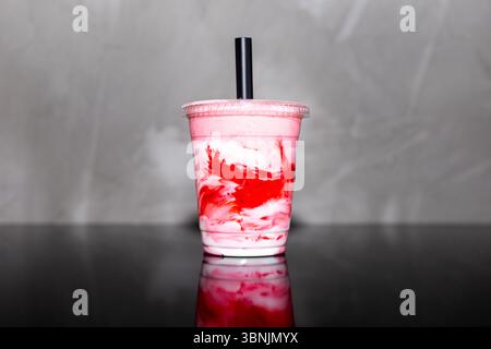 Un vibrante frullato di fragole e panna ruotato in una tazza di plastica trasparente, che riflette una scelta rinfrescante per uno stile di vita sano. Ideale per l'idratazione e Foto Stock