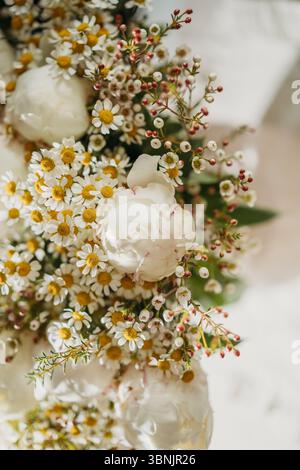 Un affascinante bouquet di margherite, peonie e fiori selvatici mostra una bellezza naturale. Questa elegante disposizione floreale trasuda romanticismo grazie alla luce soffusa Foto Stock