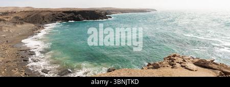 Vista panoramica della costa frastagliata e delle acque turchesi di Fuerteventura, Spagna. Le onde si infrangono dolcemente contro le coste rocciose, offrendo un ambiente tranquillo e pic-nic Foto Stock