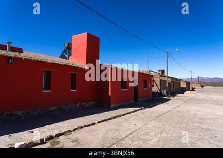 Una vibrante casa in mattoni dipinta di rosso ricco si erge sotto un cielo blu cristallino nella remota regione di la Puna in Argentina, che mostra l'architettura tradizionale Foto Stock