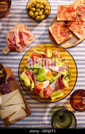 Una vivace insalata catalana con una vasta gamma di lattuga fresca, pomodori succosi, uova sode, olive e affettati assortiti, splendidamente disposti su una Foto Stock