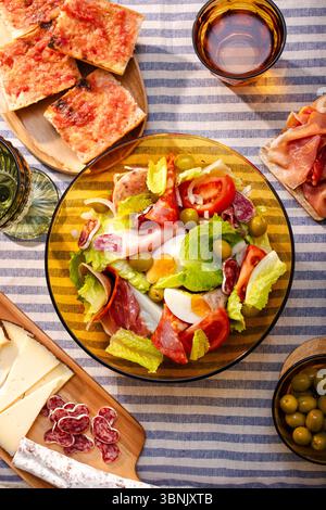 Una vivace insalata catalana con una vasta gamma di lattuga fresca, pomodori succosi, uova sode, olive e affettati assortiti, splendidamente disposti su una Foto Stock