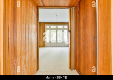 Vista attraverso un corridoio di legno che conduce ad una sala luminosa con grandi finestre in un appartamento caratterizzato da luce e calore. Foto Stock