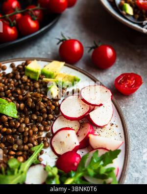 Una rinfrescante insalata estiva con lenticchie salutari, avocado maturo, croccanti ravanelli e succosi pomodori ciliegini. Condimento perfetto per un delizioso e. Foto Stock