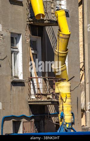 Tubo giallo per gettare le macerie da un edificio, ristrutturazione di una vecchia casa in centro città, attenzione - luogo pericoloso Foto Stock