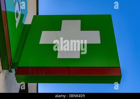 Una croce bianca su sfondo verde su uno striscione luminoso appeso alla facciata di un edificio, una farmacia, un ospedale, una clinica Foto Stock