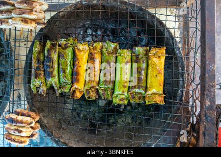 Tradizionali pacchi di foglie di banana alla griglia su una stufa a carbone nel sud-est asiatico Foto Stock