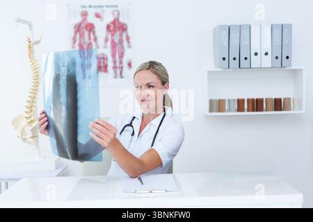 Pellicola radiografica ispezionata presso una scrivania bianca luminosa in sala clinica, con modello e leganti per colonna vertebrale Foto Stock