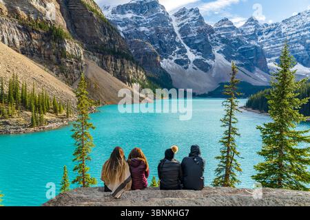 Quattro giovani donne in vacanza, sedute insieme vicino al turchese Lago Moraine, ammirando le Ten Peaks innevate. Banff National Park, Alberta, Canada Foto Stock