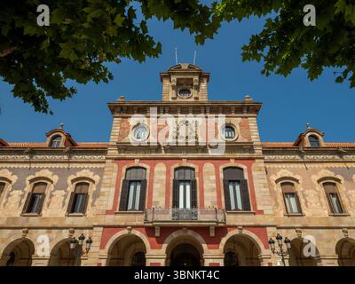 Facciata dell'edificio del Parlamento della Catalogna nel Parc de la Ciutadella, Barcellona, incorniciata da alberi, vista contro un cielo blu. Spagna. Foto Stock