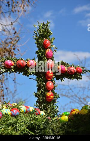 Una croce fatta di rami di bosso decorata con uova di Pasqua in cima a una fontana di Pasqua nell'alta Baviera Foto Stock