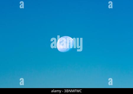 Luna piena dettagliata centrata in un cielo sereno e blu Foto Stock