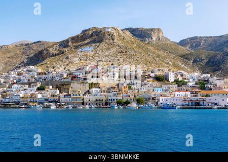 Pothia, capitale dell'isola, cappella bianca e bandiera greca dipinta sulla collina sopra Pothia con porticciolo sull'isola di Kalymnos (Kalimnos) in Grecia Foto Stock