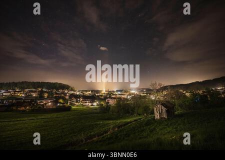 Ripresa notturna di Seekirchen am Wallersee con prato, capanna di legno, illuminazione cittadina e cielo stellato Foto Stock