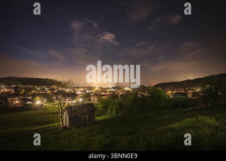 Ripresa notturna di Seekirchen am Wallersee con prato, capanna di legno, illuminazione cittadina e cielo stellato Foto Stock