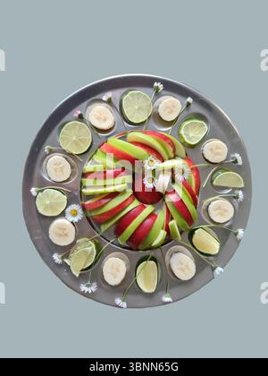 Frutta fresca su piatti da portata, nutrizione ricca di vitamine, banane sane affettate, limes e mele con buccia rossa e verde come antipasti, margherite come decorazione Foto Stock