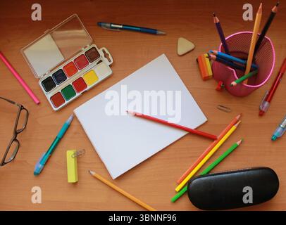 Forniture scolastiche su un tavolo di legno. Vernici ad acquerello, occhiali, penne, matite colorate. Foto Stock