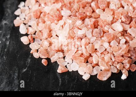 Sale rosa dell'Himalaya. Cristalli grossolani sulla superficie nera. Condimento minerale naturale. Primo piano salino sano. Ingrediente culinario per cucinare. Foto Stock