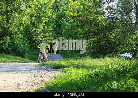 Ragazzo ucraino in bicicletta su una pista ciclabile nel parco Sumy vicino al fiume Psel. Foto Stock