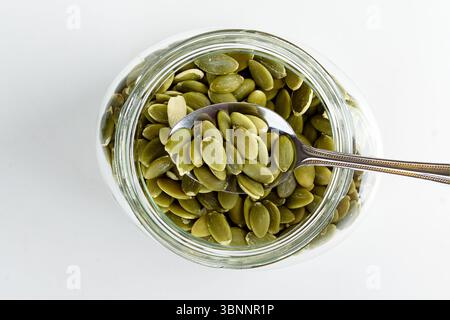Semi di zucca sgusciati su un cucchiaio sopra un barattolo di semi di zucca. Cibo sano. Foto Stock